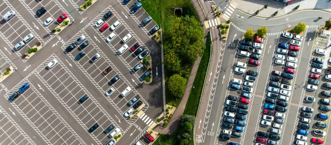 Two adjacent car parks seen from the air, one half empty and one full, separated by a line of trees
