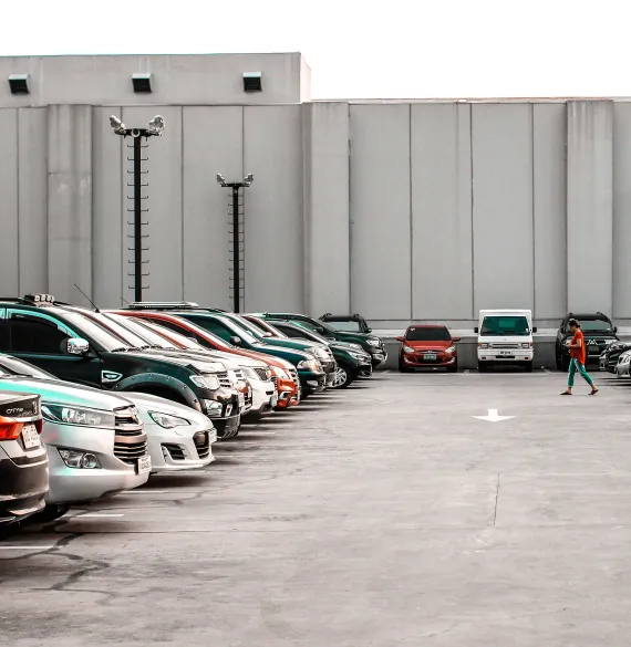 Two rows of parked cars facing a plain warehouse wall, with one person walking between them