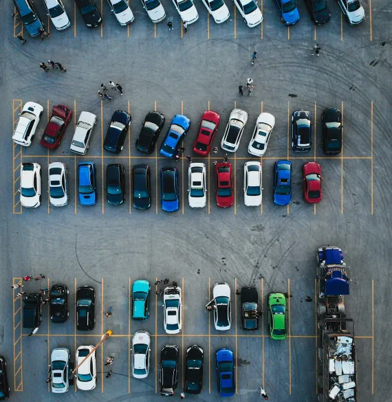A car park directly from above, with cars in yellow-marked bays and people walking between the rows